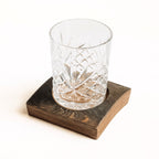 Whiskey glass on a barrel stave coaster with a white background