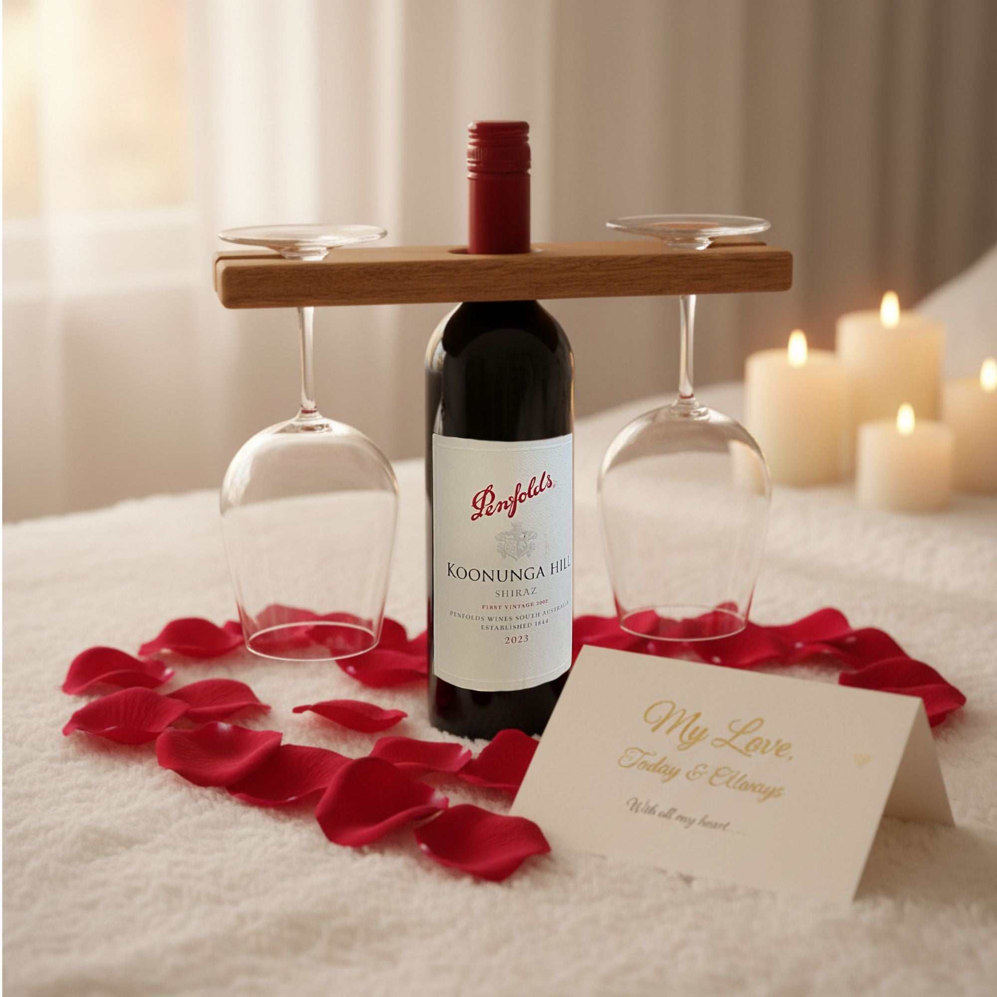 Wine butler on bottle of wine with two glasses, surrounded by red rose petals and a card on a soft surface with candles in the background
