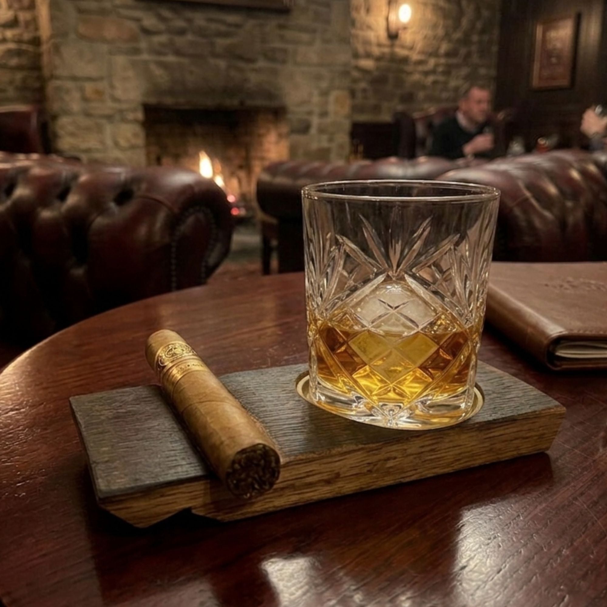 Barrel stave whisky coaster with a rocks glass of whisky and a cigar on a table